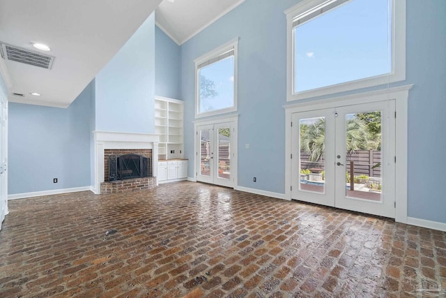 unfurnished living room featuring a brick fireplace, visible vents, baseboards, a towering ceiling, and french doors