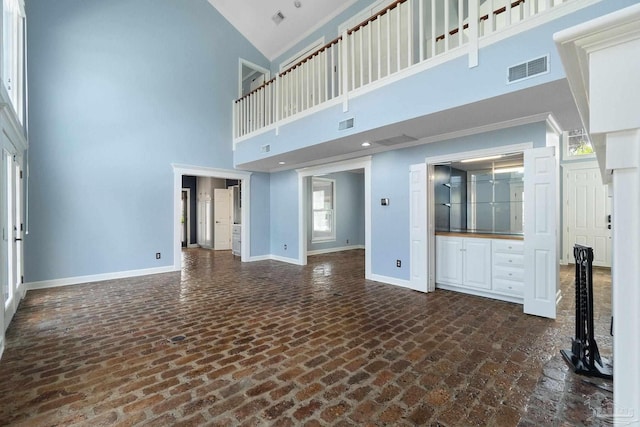 unfurnished living room with baseboards, visible vents, brick floor, and a high ceiling