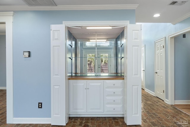 interior space featuring crown molding, visible vents, brick floor, and baseboards