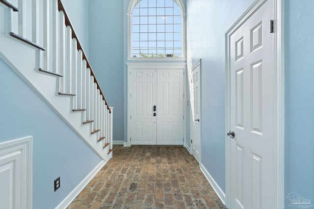 entrance foyer with stairway, brick floor, and baseboards