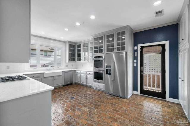 kitchen featuring gray cabinetry, a sink, brick floor, and stainless steel appliances