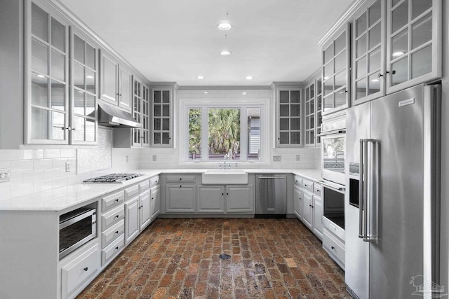 kitchen featuring brick floor, stainless steel appliances, gray cabinets, and a sink