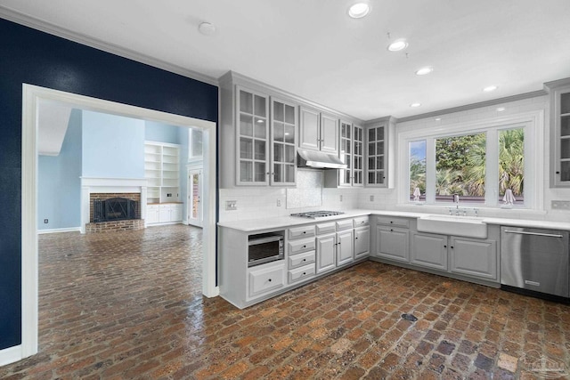 kitchen with stainless steel appliances, under cabinet range hood, brick floor, and a sink