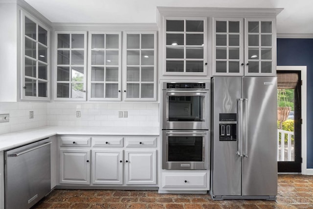 kitchen featuring stainless steel appliances, light countertops, glass insert cabinets, and backsplash