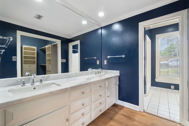 bathroom with a sink, visible vents, baseboards, ornamental molding, and wood finished floors