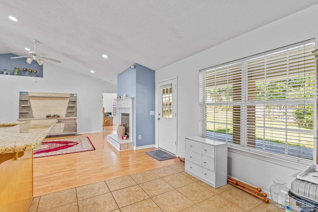 foyer with a fireplace, ceiling fan, light wood-type flooring, a textured ceiling, and lofted ceiling