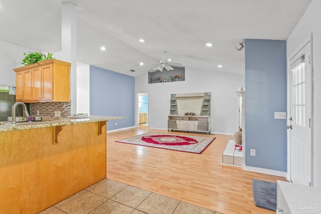 kitchen featuring tasteful backsplash, ceiling fan, light wood-type flooring, a kitchen bar, and lofted ceiling