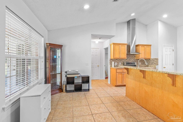 kitchen with light brown cabinetry, wall chimney exhaust hood, backsplash, and light tile patterned floors