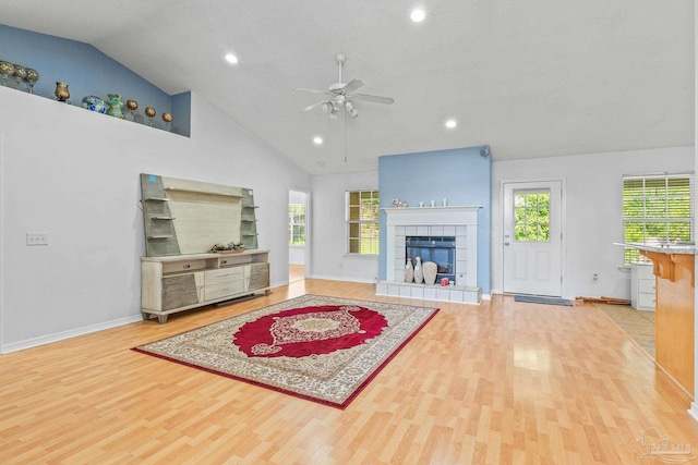 living room with a tile fireplace, high vaulted ceiling, ceiling fan, and light hardwood / wood-style floors