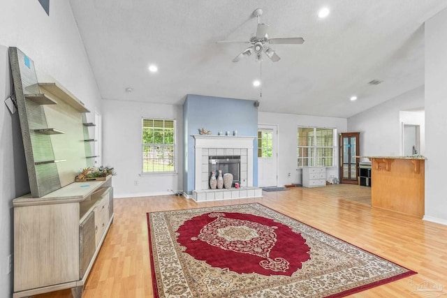 living room featuring plenty of natural light, a fireplace, light wood-type flooring, and vaulted ceiling