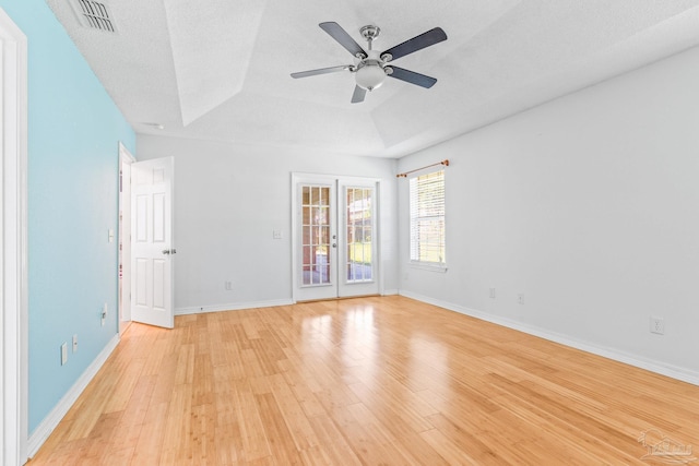 empty room featuring french doors, a textured ceiling, ceiling fan, a tray ceiling, and light hardwood / wood-style floors