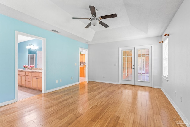 unfurnished living room with light hardwood / wood-style floors, ceiling fan, french doors, and a tray ceiling