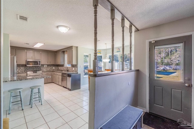 kitchen featuring kitchen peninsula, light tile patterned flooring, decorative backsplash, and appliances with stainless steel finishes