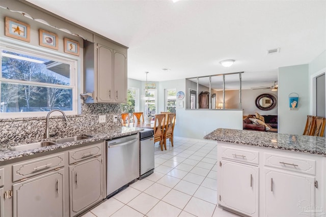 kitchen with tasteful backsplash, light tile patterned floors, stainless steel dishwasher, sink, and decorative light fixtures