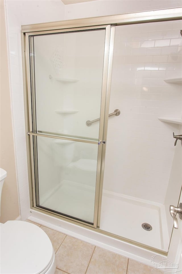 bathroom with tile patterned floors, toilet, and a shower with shower door