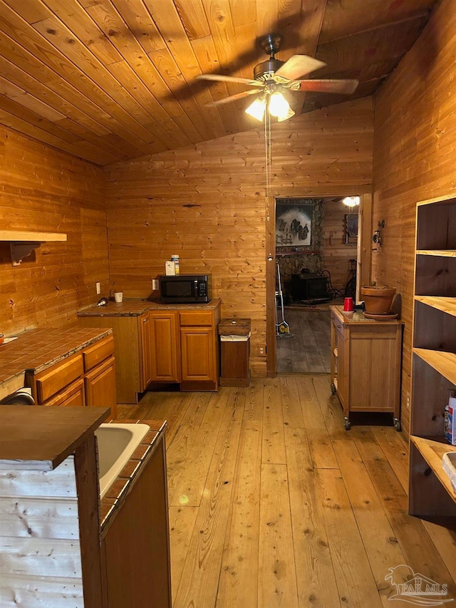 kitchen featuring wood walls, lofted ceiling, wooden ceiling, light hardwood / wood-style flooring, and ceiling fan