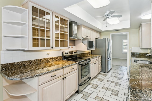 kitchen with open shelves, a sink, appliances with stainless steel finishes, wall chimney range hood, and a raised ceiling