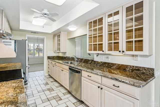 kitchen featuring glass insert cabinets, a tray ceiling, ceiling fan with notable chandelier, appliances with stainless steel finishes, and a sink