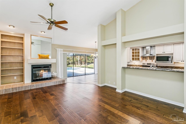 unfurnished living room with high vaulted ceiling, ceiling fan with notable chandelier, dark wood finished floors, a fireplace, and baseboards