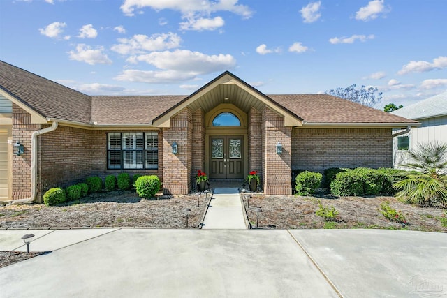 view of exterior entry with brick siding, an attached garage, and roof with shingles