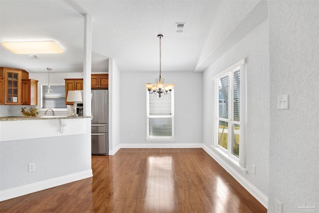 kitchen with stainless steel fridge, an inviting chandelier, dark hardwood / wood-style floors, light stone counters, and decorative light fixtures