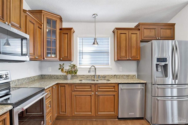 kitchen with appliances with stainless steel finishes, decorative light fixtures, sink, light hardwood / wood-style floors, and light stone counters