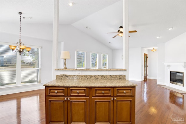 kitchen featuring decorative light fixtures, vaulted ceiling, hardwood / wood-style floors, light stone countertops, and ceiling fan with notable chandelier