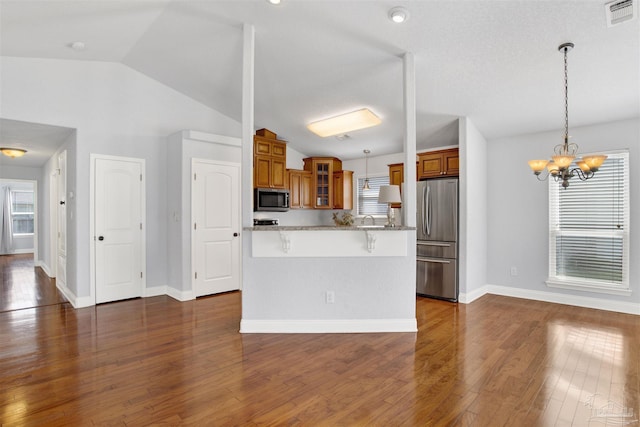 kitchen featuring appliances with stainless steel finishes, a kitchen breakfast bar, light stone countertops, dark hardwood / wood-style flooring, and decorative light fixtures