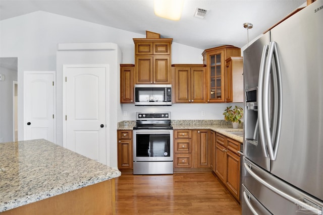 kitchen featuring pendant lighting, lofted ceiling, light stone counters, stainless steel appliances, and light wood-type flooring