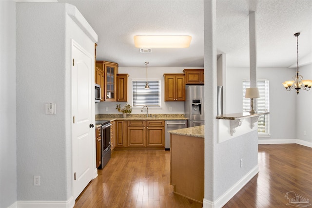 kitchen featuring appliances with stainless steel finishes, pendant lighting, sink, hardwood / wood-style flooring, and light stone countertops