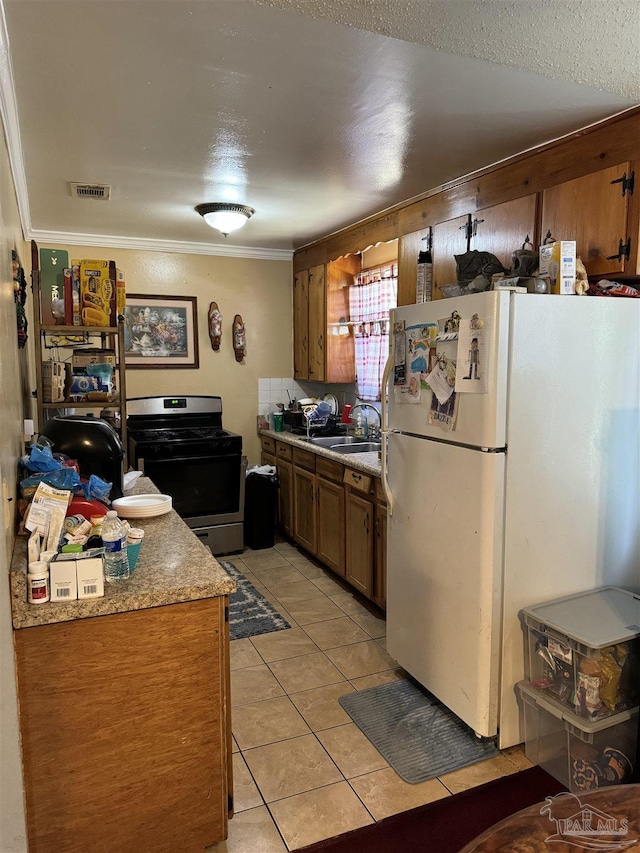 kitchen with sink, stainless steel gas range, ornamental molding, light tile patterned floors, and white fridge