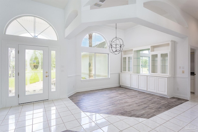 foyer with light tile patterned floors, a chandelier, plenty of natural light, and a towering ceiling