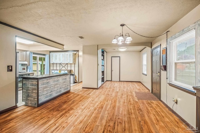 interior space with light wood-type flooring, a textured ceiling, a wealth of natural light, and an inviting chandelier