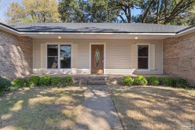 doorway to property featuring a porch, a yard, and brick siding