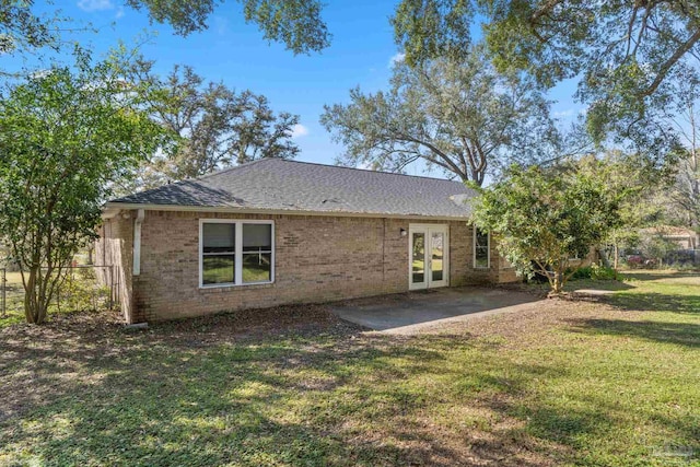 back of property featuring french doors, a yard, roof with shingles, brick siding, and a patio area