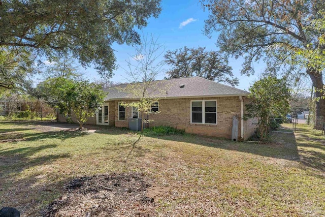 rear view of property featuring brick siding, fence, central AC unit, a lawn, and french doors