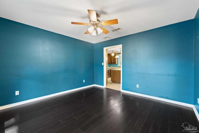 unfurnished room with wood finished floors, a ceiling fan, visible vents, and baseboards