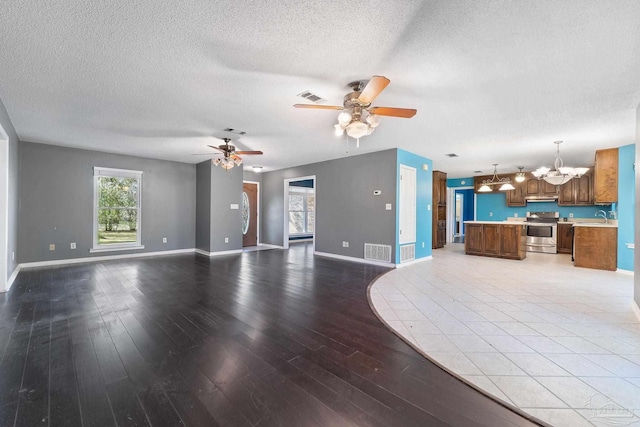 unfurnished living room featuring visible vents, ceiling fan with notable chandelier, light wood-type flooring, and a sink