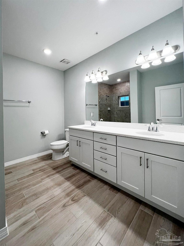 bathroom with hardwood / wood-style floors, vanity, toilet, and tiled shower