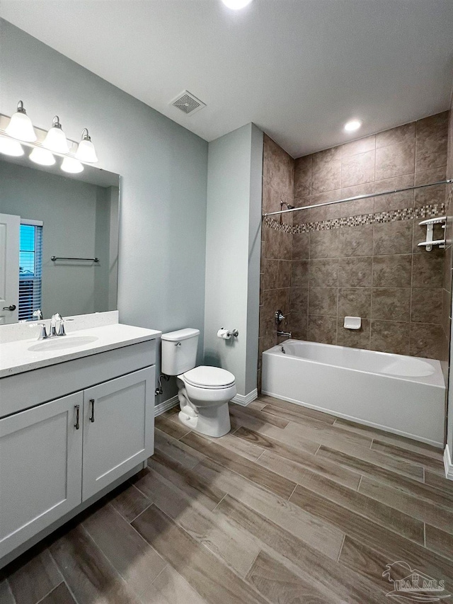 full bathroom featuring vanity, wood-type flooring, tiled shower / bath combo, and toilet