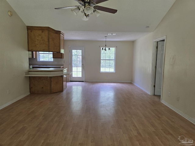 unfurnished living room featuring baseboards, light wood-style flooring, ceiling fan with notable chandelier, and vaulted ceiling