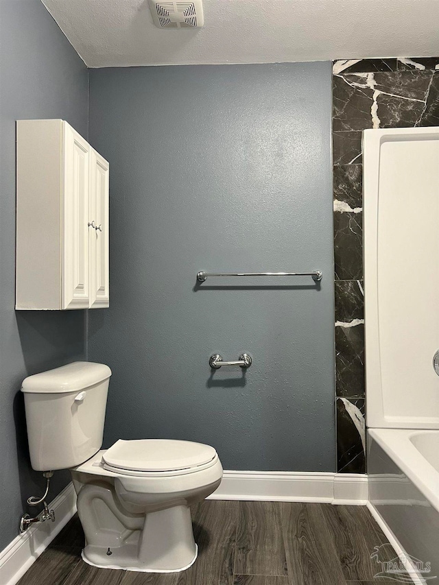 bathroom featuring hardwood / wood-style flooring, a textured ceiling, toilet, and a bathing tub