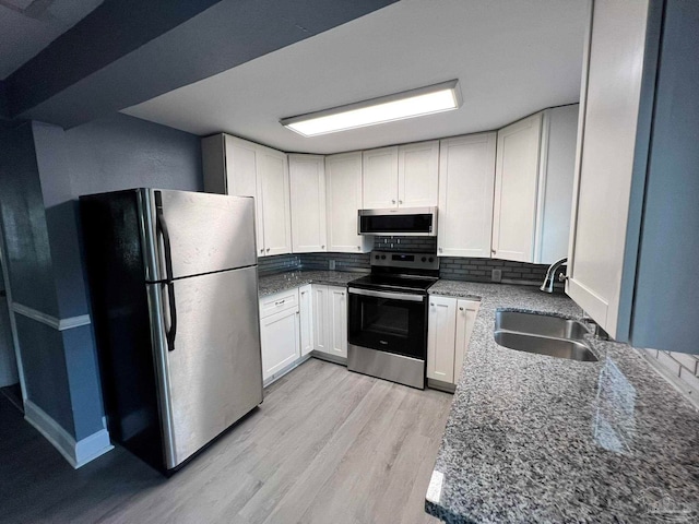 kitchen featuring stainless steel appliances, light wood-type flooring, white cabinetry, sink, and dark stone countertops