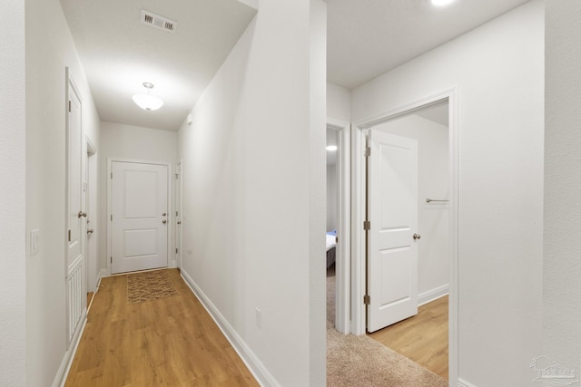 hall featuring light wood finished floors, visible vents, and baseboards