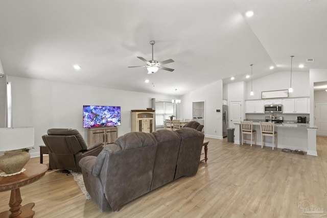 living room featuring high vaulted ceiling, light wood-style flooring, baseboards, and ceiling fan with notable chandelier