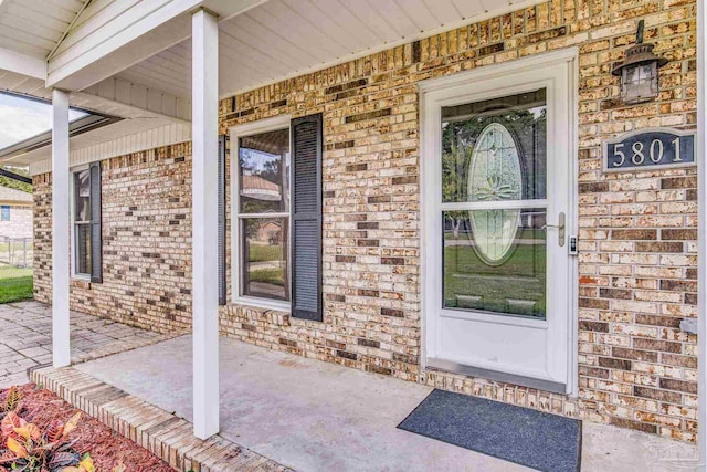 view of exterior entry featuring a porch and brick siding