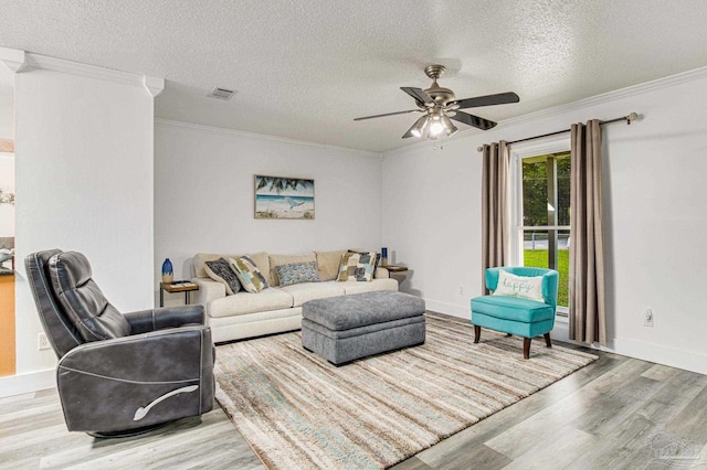 living area featuring visible vents, light wood-style flooring, ornamental molding, a textured ceiling, and ceiling fan