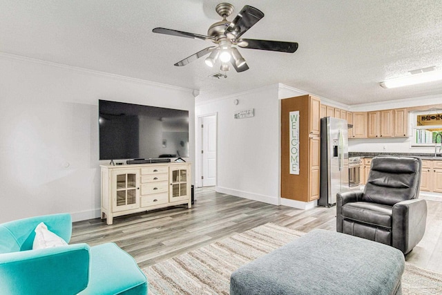 living area with a ceiling fan, baseboards, light wood finished floors, ornamental molding, and a textured ceiling