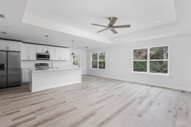 kitchen featuring hanging light fixtures, a tray ceiling, stainless steel appliances, and white cabinets