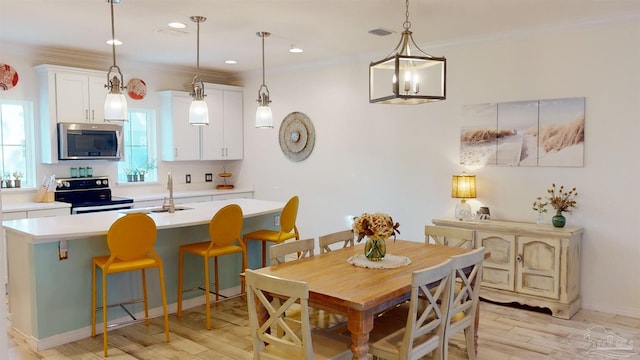 dining space with sink, ornamental molding, and light hardwood / wood-style floors